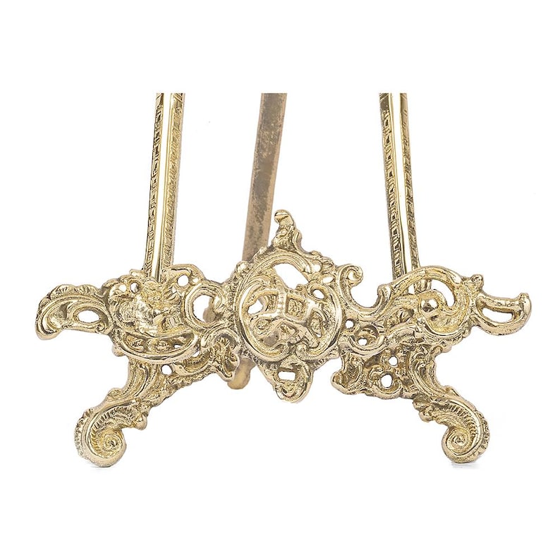 May include: A gold-colored, ornate easel with a decorative base and detailed scrollwork. The easel has a three-legged design and is made of metal. The intricate details and vintage style make it suitable for displaying artwork or photographs.