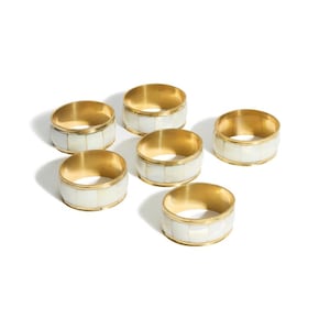 May include: Set of six gold napkin rings with white mother of pearl inlay. The rings are round and have a smooth finish.