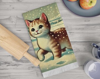 May include: A kitchen towel with a vintage illustration of a brown and white tabby cat walking through a snowy landscape. The cat has a happy expression and is surrounded by falling snowflakes.