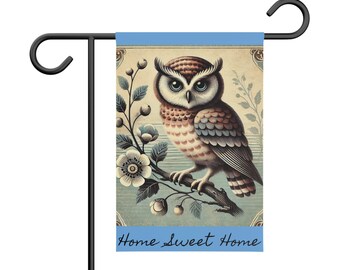 Puede incluir: Una bandera de jardín con un borde azul y una ilustración vintage de un búho posado en una rama con flores blancas. El texto "Home Sweet Home" está impreso en cursiva negra en la parte inferior de la bandera.