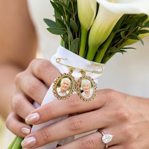 Può includere: Una spilla da balia in metallo color oro con due cornici ovali in filigrana decorata. Ogni cornice contiene una piccola fotografia ritratto di una persona anziana. La spilla è fissata su un nastro bianco avvolto attorno a un bouquet di calle.