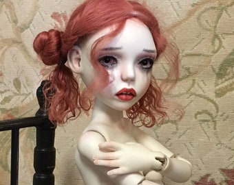 May include: A porcelain doll with red curly hair, wearing a white and gray polka dot underwear. The doll is sitting on a black wooden chair.