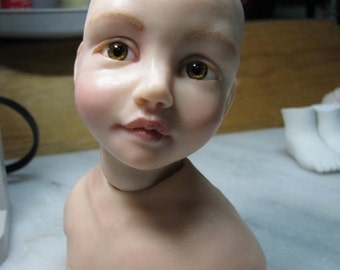 May include: A close-up of a porcelain doll head with brown eyes and a light pink complexion. The doll is wearing a white shirt and has a realistic appearance.
