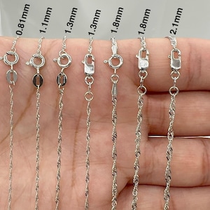 Op de afbeelding: Zeven zilveren kettingen in verschillende diktes, op een hand gelegd, met de dikte van elke ketting aangegeven in millimeters. De kettingen zijn allemaal in dezelfde stijl, met een gedraaid, touwachtig ontwerp.