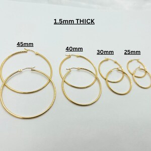 May include: Gold-colored hoop earrings in various sizes: 25mm, 30mm, 40mm, and 45mm. The text "1.5mm THICK" is displayed above the earrings. These earrings are a classic jewelry staple.