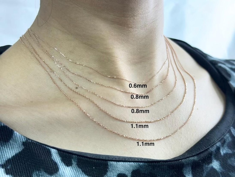 May include: Five gold chains of different thicknesses, layered on a person's neck. The chains are labeled with their thickness in millimeters: 0.6mm, 0.8mm, 0.8mm, 1.1mm, and 1.1mm.