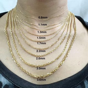 Könnte beinhalten: Nahaufnahme einer Person, die verschiedene goldene Kettenhalsketten trägt, jede mit einer anderen Dicke. Die Ketten sind mit ihrer Dicke in Millimetern beschriftet, von 0,8 mm bis 3,6 mm.