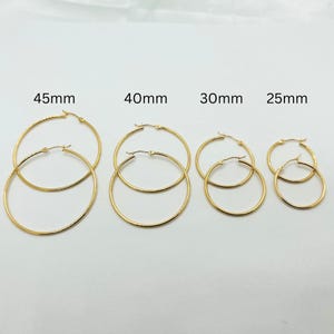 May include: Four pairs of gold-colored hoop earrings in various sizes. The sizes are labeled as 45mm, 40mm, 30mm, and 25mm. Each pair has a simple, classic design with a hinged closure.
