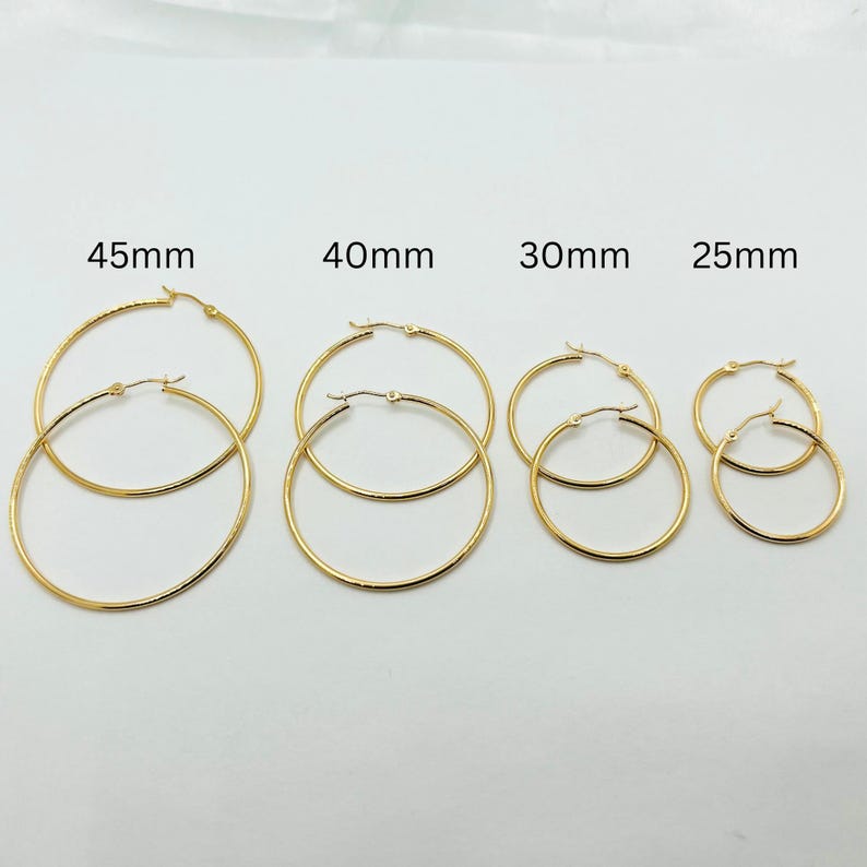 May include: Four pairs of gold-colored hoop earrings in various sizes. The sizes are labeled as 45mm, 40mm, 30mm, and 25mm. Each pair has a simple, classic design with a hinged closure.