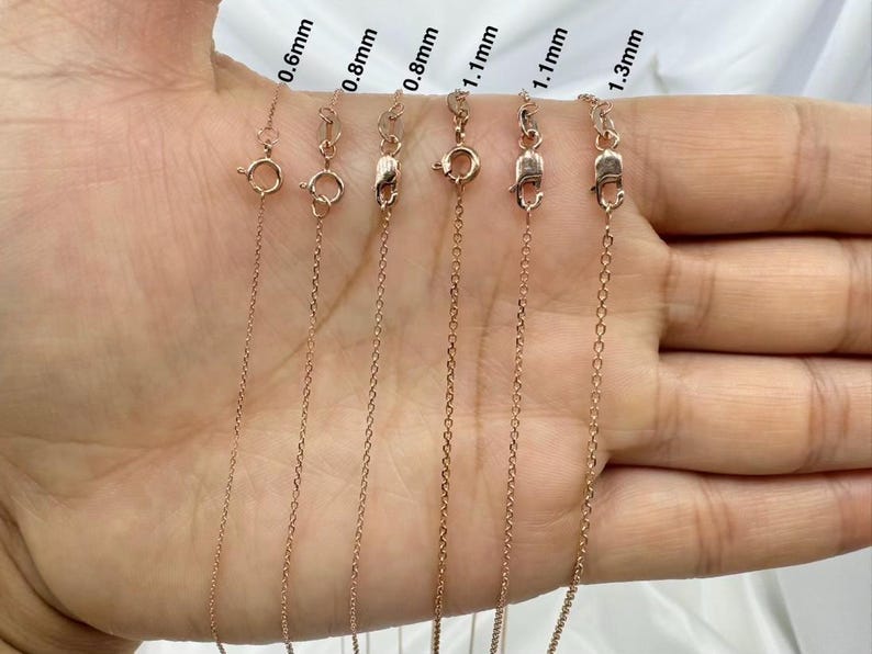 May include: A close-up of six gold chains of different thicknesses, ranging from 0.6mm to 1.3mm. The chains are laid out on a hand, with the thickness of each chain labeled.