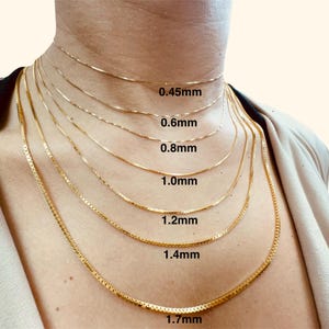 May include: A close-up of a model wearing seven gold chain necklaces of varying widths, labeled with their thickness in millimeters: 0.45mm, 0.6mm, 0.8mm, 1.0mm, 1.2mm, 1.4mm, and 1.7mm.