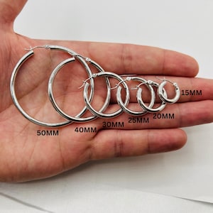 May include: A set of six silver hoop earrings in varying sizes, from 15mm to 50mm. Each earring is a simple, polished metal circle with a hinged closure. The sizes are labeled on the image.