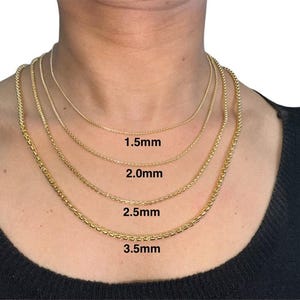 Pode incluir: São exibidas quatro correntes douradas de diferentes espessuras. As correntes estão rotuladas como 1,5 mm, 2,0 mm, 2,5 mm e 3,5 mm. Os colares são usados ​​em volta do pescoço de uma pessoa, mostrando os diferentes estilos e tamanhos das correntes.