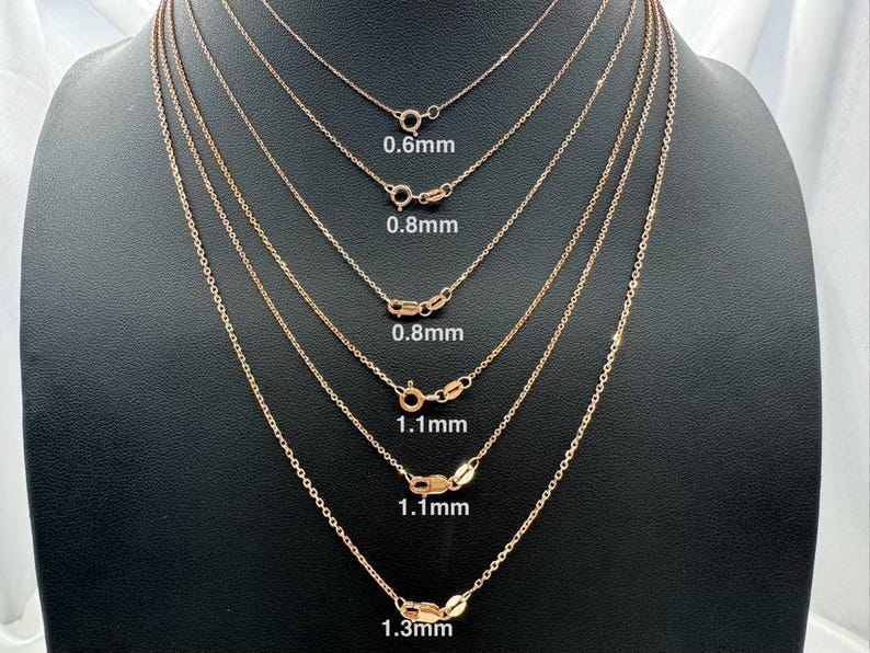 May include: Six gold chains of different thicknesses, hanging from a display stand. The chains are labeled with their thickness in millimeters: 0.6mm, 0.8mm, 0.8mm, 1.1mm, 1.1mm, and 1.3mm.