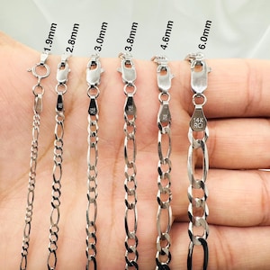 May include: Six silver chains of different widths, ranging from 1.9mm to 6.0mm, are displayed on a hand. The chains are all made of 14k gold and have a classic figaro design.