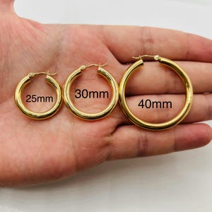 May include: Three gold-colored hoop earrings in varying sizes: 25mm, 30mm, and 40mm. The earrings are round with a polished finish. The image shows the earrings against a neutral background.