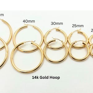 May include: A collection of gold hoop earrings in various sizes, ranging from 15mm to 50mm. The earrings are displayed on a white surface, with the sizes labeled above each pair. The text "14k Gold Hoop" is at the bottom.