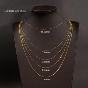 Puede incluir: Cinco cadenas de caja de oro de diferentes grosores en un maniqu&iacute; negro. Las cadenas est&aacute;n etiquetadas con su grosor en mil&iacute;metros: 0,45 mm, 0,6 mm, 0,8 mm, 1,0 mm y 1,4 mm. Cadena de caja de oro de 10 quilates.
