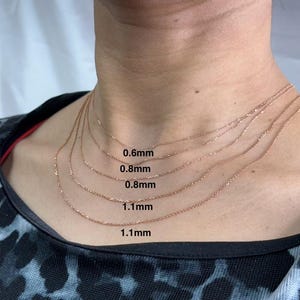 May include: Five gold chains of different thicknesses are layered on a person's neck. The chains are labeled with their thickness in millimeters: 0.6mm, 0.8mm, 0.8mm, 1.1mm, and 1.1mm.