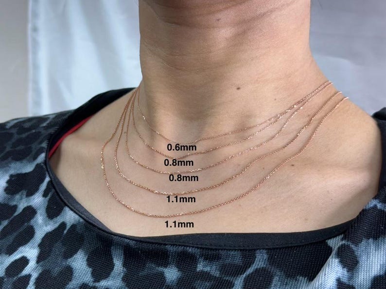 May include: Five gold chains of different thicknesses are layered on a person's neck. The chains are labeled with their thickness in millimeters: 0.6mm, 0.8mm, 0.8mm, 1.1mm, and 1.1mm.
