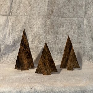 May include: Three wooden Christmas tree ornaments in various sizes. The trees are dark brown with a wood grain pattern.