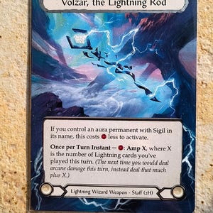 Puede incluir: Carta coleccionable "Volzar, the Lightning Rod" con fondo azul y blanco con rayos. El texto de la carta describe sus habilidades. La carta es una "Lightning Wizard Weapon - Staff (2H)".