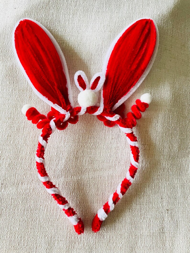 May include: A red and white bunny ear headband. The ears are red with white trim, and the headband is red and white twisted. A small white bunny face is centered between the ears. This festive accessory is perfect for Easter or themed events.
