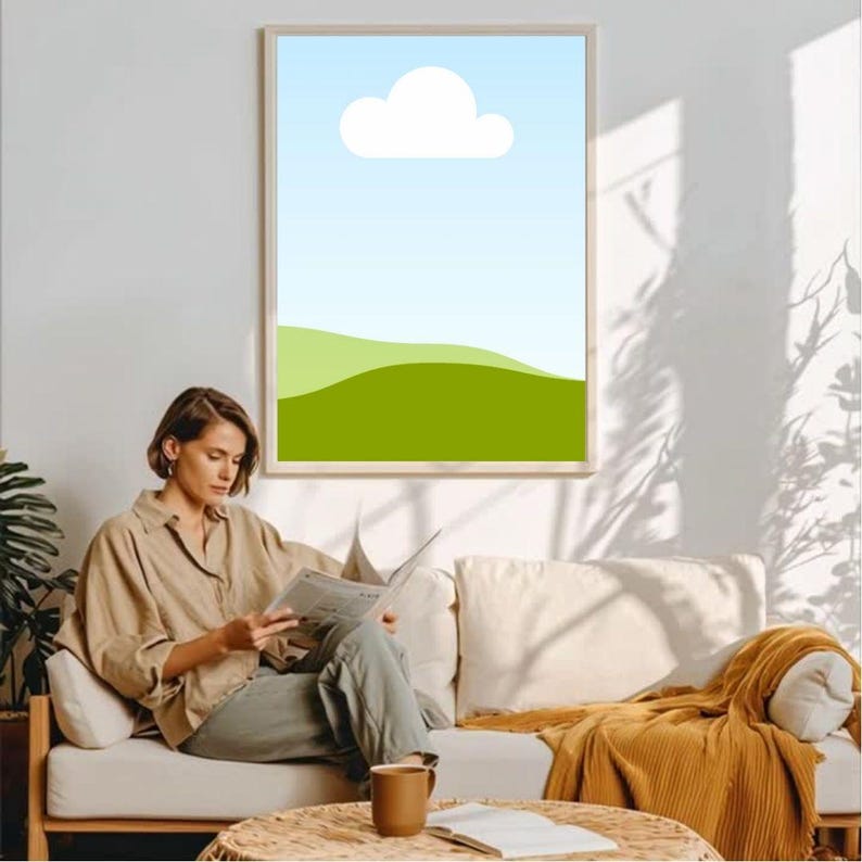 Puede incluir: Una impresi&oacute;n art&iacute;stica enmarcada que representa un paisaje con un cielo azul, una nube blanca y colinas verdes. La obra de arte est&aacute; sobre un sof&aacute; donde una mujer lee un peri&oacute;dico. Una taza marr&oacute;n descansa sobre una peque&ntilde;a mesa.