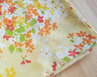 Pode incluir: Um lençol de tecido amarelo dobrado com um padrão floral em tons de laranja, vermelho e verde. As flores são pequenas e espalhadas pelo tecido.