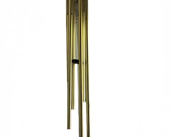 May include: A gold-colored wind chime with multiple cylindrical tubes suspended from a dark brown hexagonal top. A black triangular piece hangs at the bottom. The chimes are designed for outdoor decor.