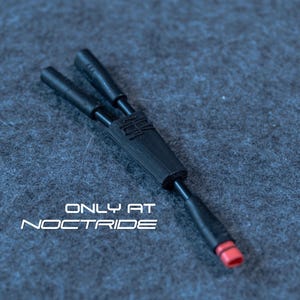 Op de afbeelding: Een zwarte Y-splitterkabel met twee connectoren en een enkele connector met een rode punt. De tekst "ONLY AT NOCTRIDE" is in het wit gedrukt. De kabel ligt op een getextureerd, donkergrijs oppervlak.