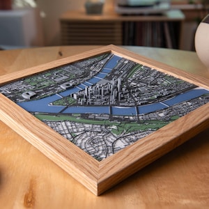 May include: A framed 3D map of a city, featuring a detailed representation of buildings, roads, and waterways. The map is set within a natural wood frame, showcasing a modern and artistic design. The city map is a unique piece of home decor.