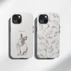 May include: Two white iPhone cases with a black and white rabbit design. One case has the name "Abigail" printed on it and the other case has the name "Maria" printed on it.