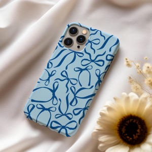 May include: A light blue phone case with a pattern of blue bows. The case has a camera lens cutout in the upper left corner.