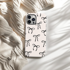 May include: A white phone case with a black bow pattern. The case has a camera lens cutout and a white background.