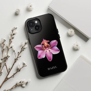 May include: Black phone case featuring a pink orchid flower design with the word "HAZEL" printed at the bottom.