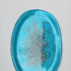 May include: A turquoise blue oval glass dish with a white and gray speckled design. The design resembles a tree or a burst of light.