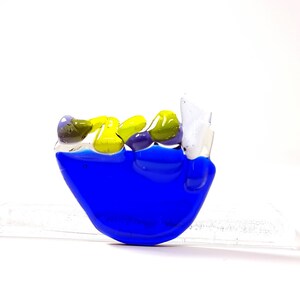 May include: A blue glass sculpture of a boat with yellow and purple glass pieces inside. The boat is sitting on a white surface.