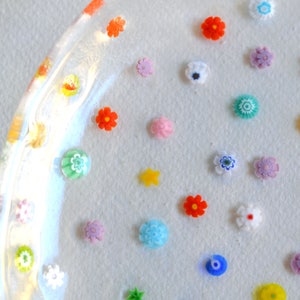 Puede incluir: Un plato de vidrio transparente adornado con numerosas flores de vidrio peque&ntilde;as y coloridas. Las flores, en tonos de rojo, azul, amarillo y blanco, son de diversos dise&ntilde;os y est&aacute;n dispersas sobre la superficie del plato.