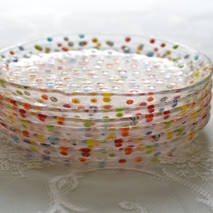 Puede incluir: Una pila de platos de vidrio transparente con lunares de colores. Los platos tienen un borde ligeramente ondulado y est&aacute;n apilados uno encima del otro. Los puntos son de varios colores, incluyendo rojo, amarillo, azul y verde. Los platos son un art&iacute;culo decorativo.