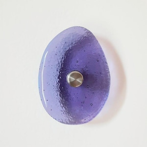 Peut inclure: Bouton de meuble ovale en verre violet fait à la main. Il présente une surface texturée avec de petites bulles d'air et une vis en métal brossé. Le design est simple et élégant.