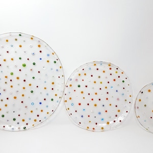 Puede incluir: Tres platos de vidrio transparente de diferentes tama&ntilde;os, adornados con puntos de colores espaciados uniformemente. Los puntos son rojos, amarillos, verdes y azules. Los platos est&aacute;n dispuestos sobre un fondo blanco.