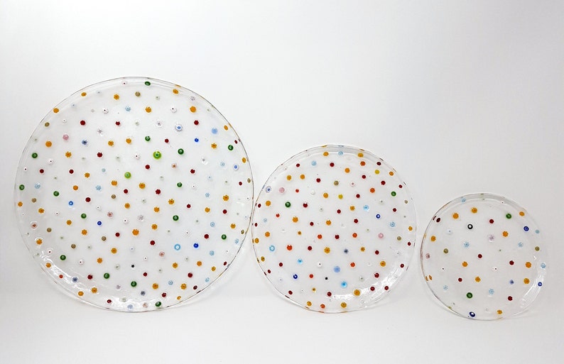 Puede incluir: Tres platos de vidrio transparente de diferentes tama&ntilde;os, adornados con puntos de colores espaciados uniformemente. Los puntos son rojos, amarillos, verdes y azules. Los platos est&aacute;n dispuestos sobre un fondo blanco.