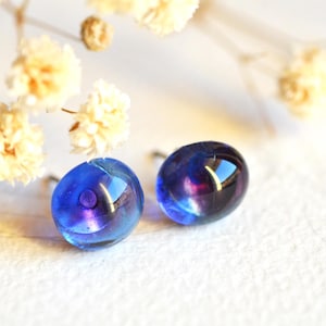 May include: A pair of iridescent blue and purple glass stud earrings. The earrings are round and have a reflective surface.