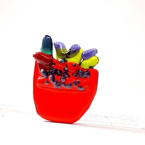 May include: A red glass sculpture of a flower pot with colorful flowers. The flowers are made of glass and are in shades of purple, yellow, and green.