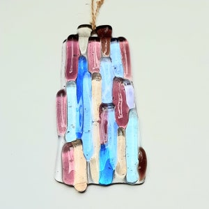 May include: A glass ornament with a mosaic design featuring shades of pink, blue, and cream. The ornament is shaped like a rectangle and has a string for hanging.