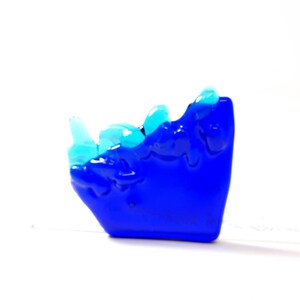 May include: A blue glass sculpture with a wave-like design. The top of the sculpture is made of clear glass with a light blue tint.