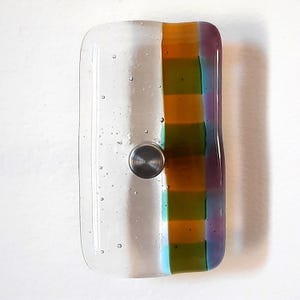 May include: A rectangular glass cabinet knob featuring a clear section with small air bubbles on the left and a vertical striped pattern in orange, green, and purple on the right, centered with a circular brushed metal mounting hardware piece.