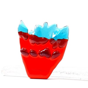 May include: A red and blue glass sculpture with a jagged, flame-like shape. The sculpture is made of glass and has a textured surface.