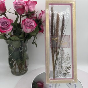 May include: A bouquet of pink roses with red edges in a clear glass vase. Next to the vase is a rectangular glass display case with dried plants and the words "make today" printed on it.